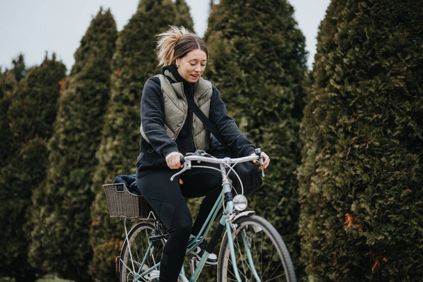 Una gioiosa giovane ciclista donna che cavalca con un sorriso tra il verde lussureggiante in un tranquillo parco, evocando libertà e stile di vita sano. - Foto, immagini