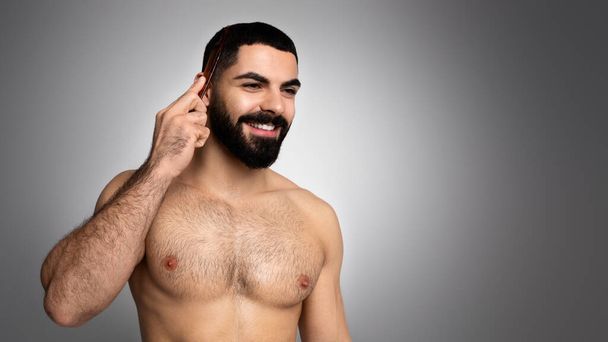 ヘアケア,男性のための健康的な髪の成長,美容治療の概念. ハッピーハンサムな半裸のアラブの男は,コピースペース,灰色の背景を見ながら,ブラシと微笑んで髪をかぶっています - 写真・画像