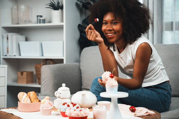 Mooie jonge Afrikaanse blogger presenteren stuk cupcake in concept met speciale keuken in pastelkleur. Content creëren van sociale media met favoriete snoep bakkerij schotel. Smaakstof. - Foto, afbeelding