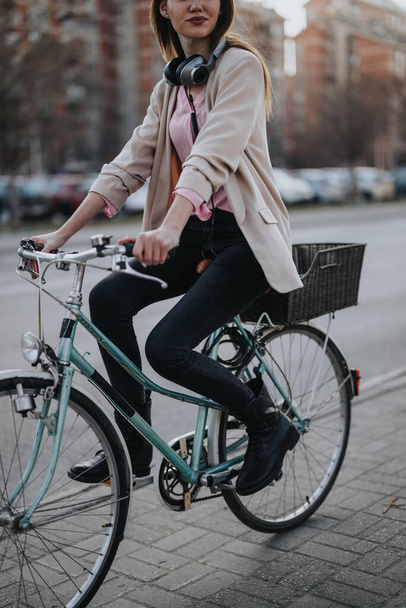 Элегантная молодая женщина на ретро-велосипеде в городской обстановке, в пиджаке и наушниках, воплощающая активный образ жизни и экологичный транспорт. - Фото, изображение
