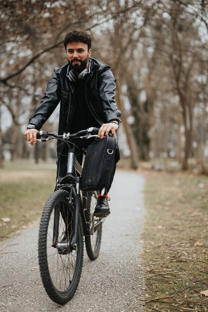 Όμορφος γενειοφόρος επιχειρηματίας σε εξωτερικούς χώρους με ποδήλατο, εργάζεται εξ αποστάσεως σε αστικό πάρκο. - Φωτογραφία, εικόνα