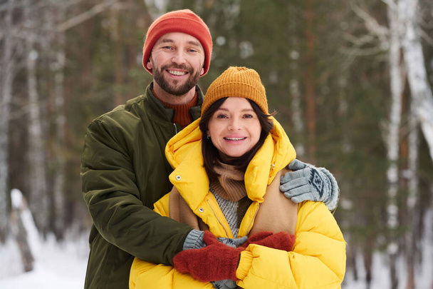Μέτριο πορτραίτο του ευτυχισμένου Καυκάσου άνδρα και γυναίκα ερωτευμένη στέκεται σε εξωτερικούς χώρους χαμογελώντας στην κάμερα την ημέρα του χειμώνα - Φωτογραφία, εικόνα