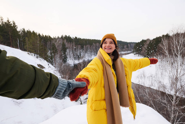 POV de hombre irreconocible cogido de la mano de su alegre esposa siguiéndola mientras caminaba en las montañas en el día de invierno - Foto, imagen