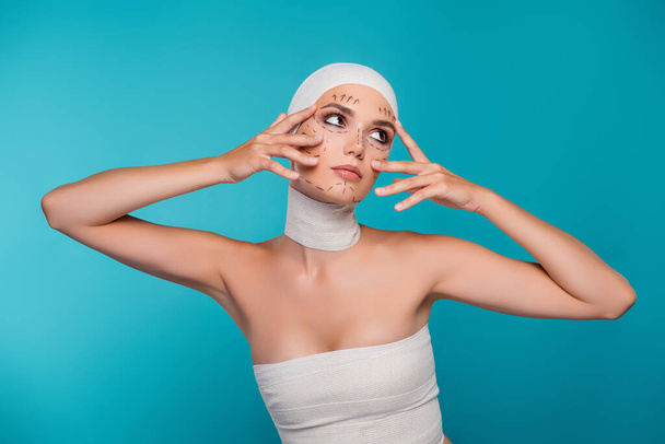 Kuva houkutteleva nainen lääketieteellinen side valmistautua plastiikkakirurgia touch silmät iho näyttää yli syaani tausta. - Valokuva, kuva