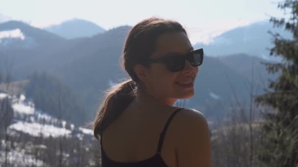 Szemüveges lány mosolyog a kamerába, és elfordul, hogy megfigyelje a nyugodt hegyvonulatot tavasszal. - Felvétel, videó
