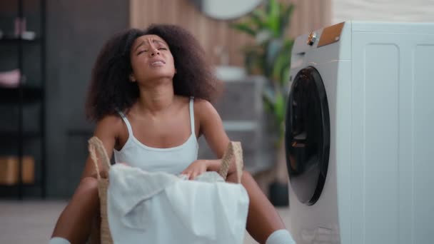 Wütend traurig Frau verärgert irritiert müde frustriert Afroamerikanerin ethnisch weiblich birassisch Hausfrau erschöpft mit Hausaufgaben schmutzige Kleidung Wut mit Wäsche zu Hause Waschmaschine Haushalt - Filmmaterial, Video