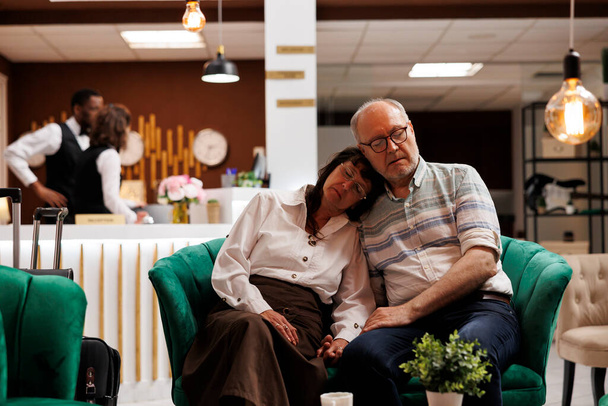 Wyczerpane piękne starsze pary śpią na wygodnych kanapach w luksusowym hotelowym lobby. Czekając na odprawę, emeryci starsi podróżnicy ucinają sobie drzemkę w salonie po długim locie. - Zdjęcie, obraz