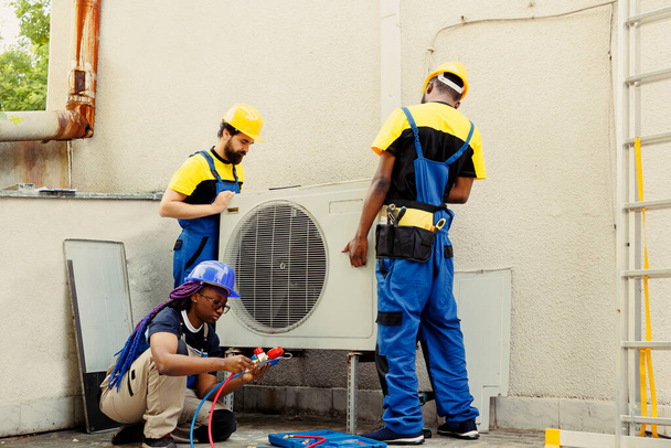 Diverse team van doorgewinterde draadwerkers installeren van nieuwe externe airconditioner voor de klant. Licensed servicemedewerkers belast met het optimaliseren van nieuwe HVAC-systemen prestaties, ervoor te zorgen dat het draait op perfecte efficiëntie - Foto, afbeelding