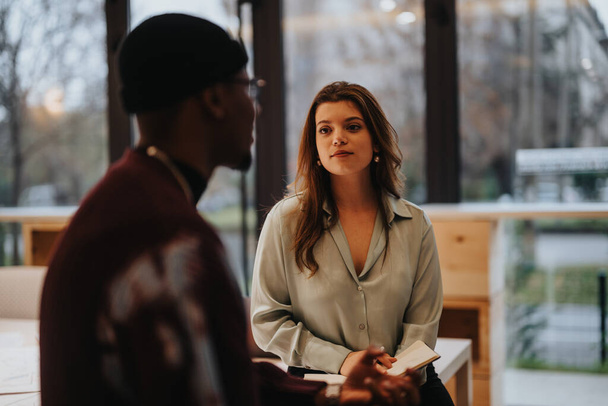 A focused young businesswoman in a casual office sitting attentively across from a male colleague during a collaborative discussion. Soft focus on the man in the foreground. - Photo, Image