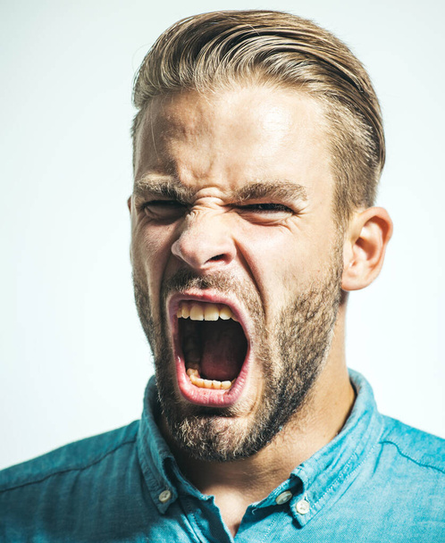 Retrato de primer plano del hombre enojado disgustado gritando. Un hombre furioso con la boca abierta a gritos. Estrés y emociones negativas. Rabia y concepto agresivo. Varón barbudo en camisa de mezclilla gritando de rabia - Foto, imagen