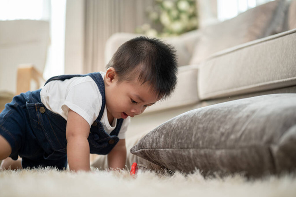 Un simpatico, allegro bambino asiatico sta giocando con i giocattoli e strisciando sul pavimento nel soggiorno. bambino, infanzia, bambino, figlio piccolo - Foto, immagini