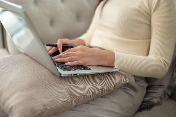 Una foto recortada de una mujer de negocios se centra en su computadora portátil en un sofá en su sala de estar, trabajando remotamente en casa. - Foto, Imagen
