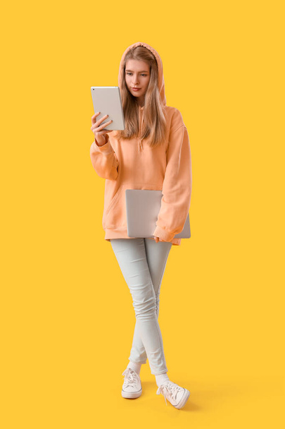 Female programmer with tablet computer and laptop on yellow background - Photo, Image