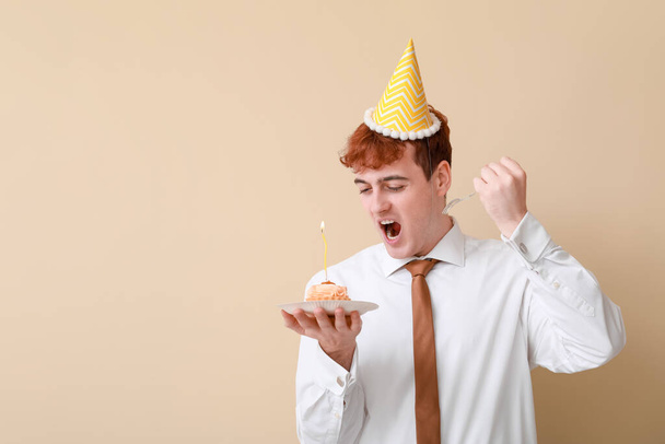 Angry young man with piece of birthday cake on beige background - Photo, Image
