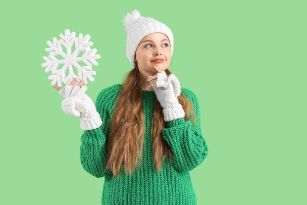 Beautiful thoughtful young woman in warm clothes with decorative snowflake on green background - Photo, Image