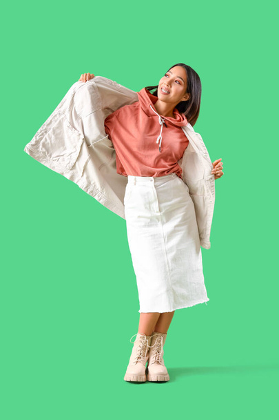 Νεαρή Ασιάτισσα με κουκούλα και βαμβακερό μπουφάν σε πράσινο φόντο - Φωτογραφία, εικόνα