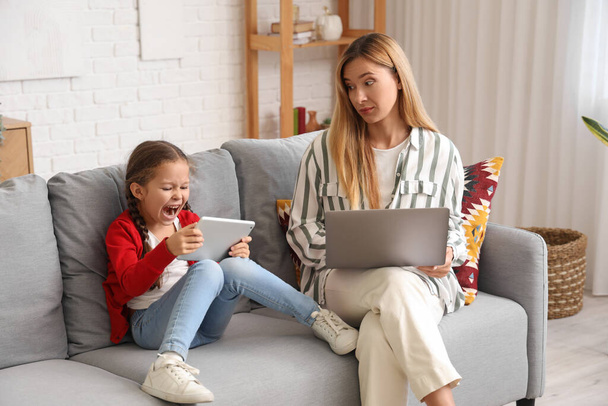 Работая молодая женщина подчеркнула, что ее шумная маленькая дочь с планшетным компьютером дома - Фото, изображение