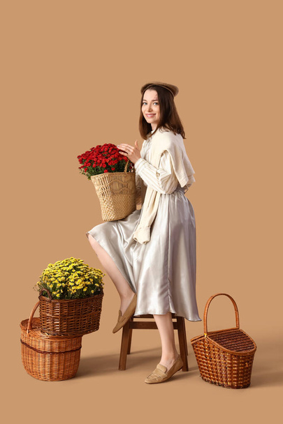 Young woman with chrysanthemum flowers on beige background - Фото, зображення