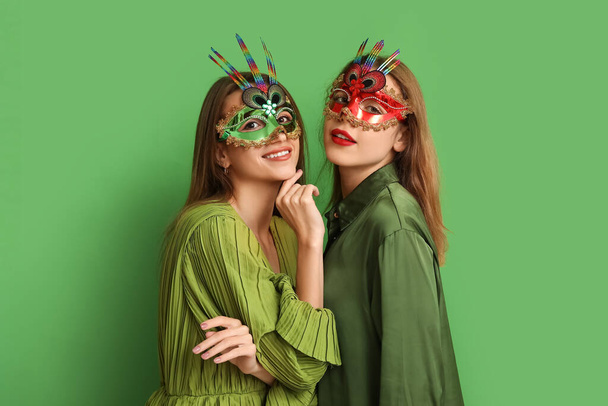 Красиві молоді жінки в карнавальних масках на зеленому тлі - Фото, зображення