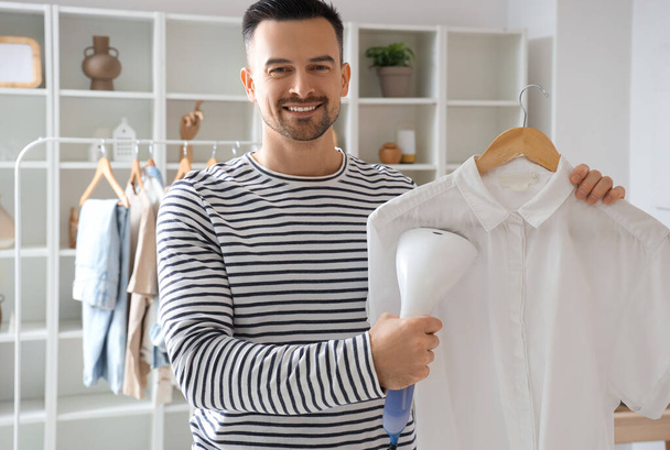 Schöner Mann dampfendes Hemd mit modernem Dampfer zu Hause - Foto, Bild