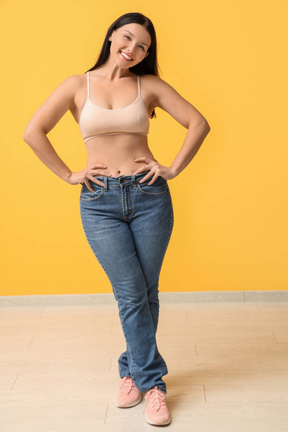 黄色の背景に新しいジーンズで美しい若い幸せな女性. 減量コンセプト - 写真・画像