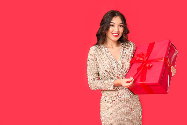 Beautiful young happy Asian woman with gift box on red background. Valentine's Day celebration - Photo, Image