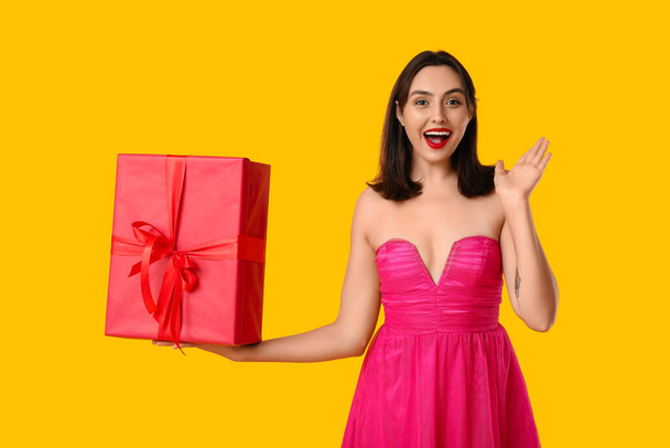 黄色の背景にギフトボックスを持つ美しい若い幸せな女性. バレンタインデーのお祝い - 写真・画像