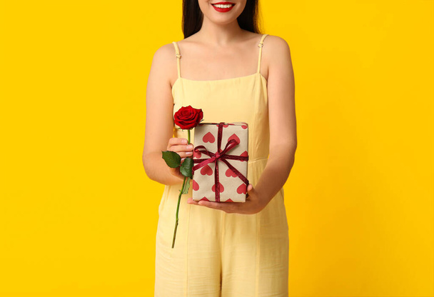 Mulher bonita com caixa de presente e rosa vermelha no fundo amarelo. Celebração do Dia dos Namorados - Foto, Imagem