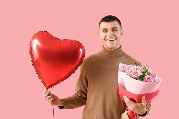 Όμορφος νεαρός άνδρας με μπαλόνι σε σχήμα καρδιάς και μπουκέτο λουλούδια για την ημέρα του Αγίου Βαλεντίνου σε ροζ φόντο - Φωτογραφία, εικόνα