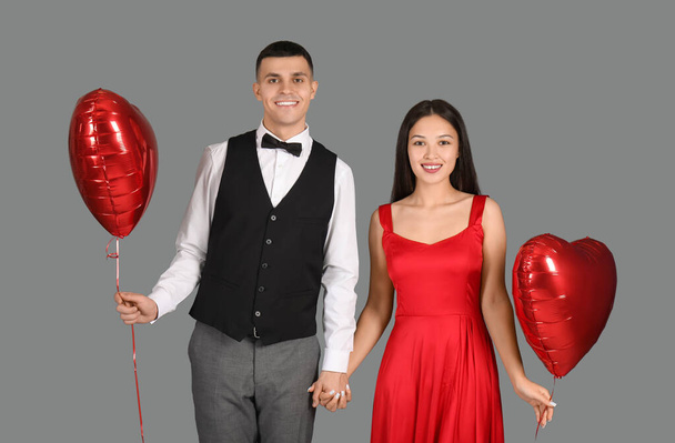 Young couple with heart-shaped air balloons for Valentine's day holding hands on grey background - Photo, Image