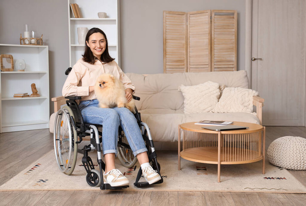 Feliz joven en silla de ruedas con perro Pomerania en casa - Foto, Imagen