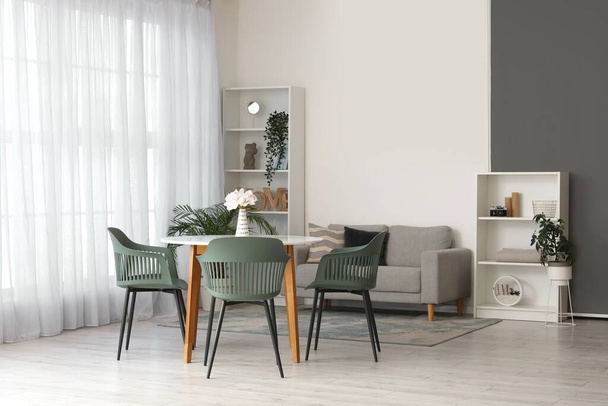 Интерьер удобной гостиной со столом, стульями, комнатными растениями, диваном и полками - Фото, изображение