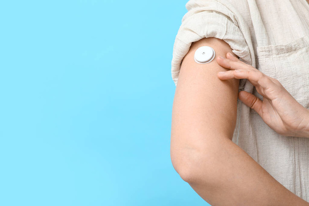 Woman with glucose sensor for measuring blood sugar level on blue background, closeup. Diabetes concept - Photo, Image