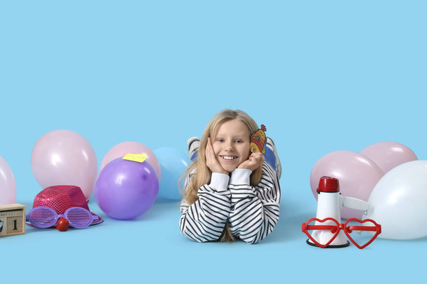 Grappig klein meisje met decor en ballonnen liggend op blauwe achtergrond. April Feestdag voor dwazen - Foto, afbeelding