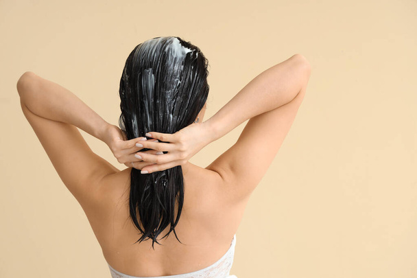 Jovem mulher aplicando máscara de cabelo no fundo bege, visão traseira - Foto, Imagem