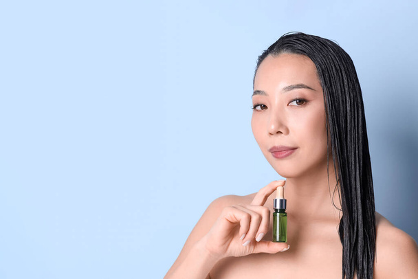 Mooie Aziatische vrouw met fles van haar olie op blauwe achtergrond, close-up - Foto, afbeelding