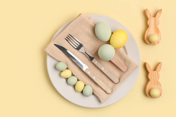 Красивая сервировка стола с пасхальными яйцами и деревянными кроликами на желтом фоне - Фото, изображение