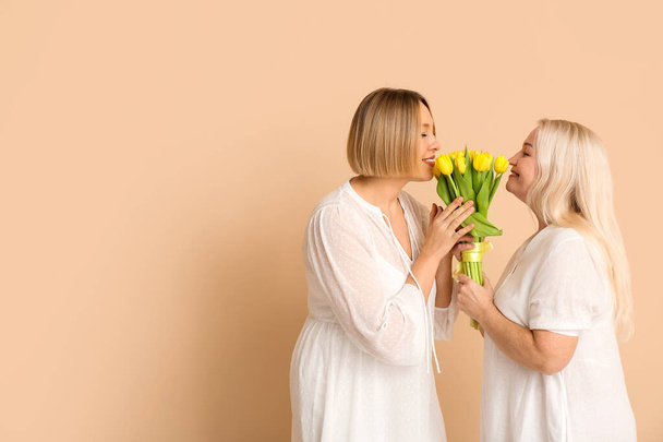 Volwassen vrouw begroet haar moeder met boeket tulpen op beige achtergrond. Internationale Vrouwendag viering - Foto, afbeelding
