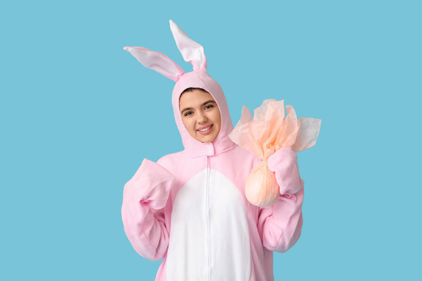 Belle jeune femme en costume de lapin avec oeuf cadeau de Pâques sur fond bleu - Photo, image
