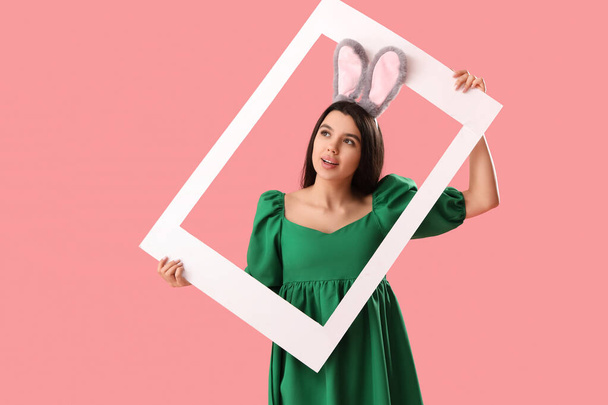 Mooie jonge vrouw in konijnenoren met frame op roze achtergrond. Pasen viering - Foto, afbeelding