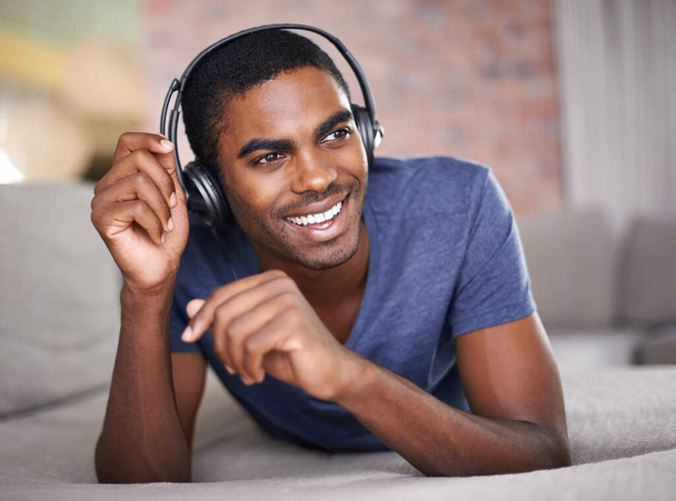 Man, portret en glimlach met muziek op de bank voor audio streaming, podcast of headset in de woonkamer van thuis. Student, zwarte persoon of gezicht met hoofdtelefoon voor ontspanning, radio-abonnement of rust op de bank. - Foto, afbeelding