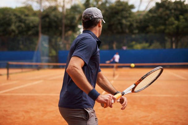 Tennis, training and man in game of sport, competition or exercise for fitness on court. Athlete, workout and play on pitch outdoor in summer with action, challenge and person in contest from back. - Photo, Image