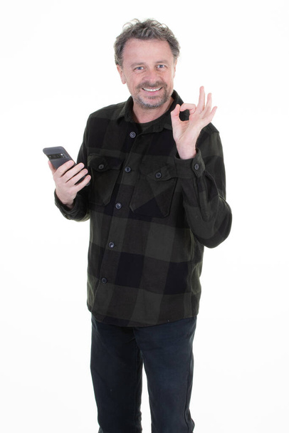Mutlu gülümseyen orta yaşlı adam işaret parmağını beyaz arka planda asılı akıllı telefondan yapıyor. - Fotoğraf, Görsel
