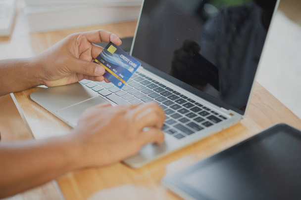 Close Up человек держит в руках кредитную карту, используя онлайн-покупки с ноутбука, онлайн-платежи дома или в офисе, интернет-банкинг, идеи будущего образа жизни для расходов или предпринимателей при заказе продуктов - Фото, изображение