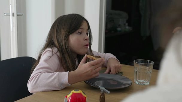 Una niña comiendo durante la hora de la comida interactuando con la familia fuera de cámara. Snacking infantil esfiha - Foto, imagen