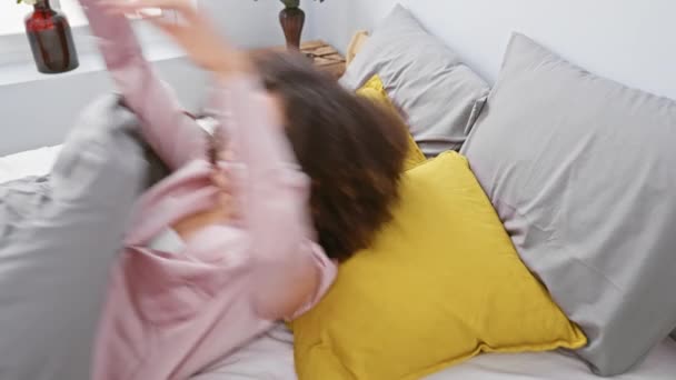 Een jonge vrouw met krullend haar genietend van een ontspannen ochtend in een moderne slaapkamer. - Video