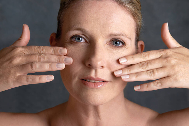 Portrait, beauty and hands with mature woman in studio on gray background for aesthetic wellness. Face, relax and touching with natural skin person at spa for antiaging cosmetics or treatment. - Fotoğraf, Görsel