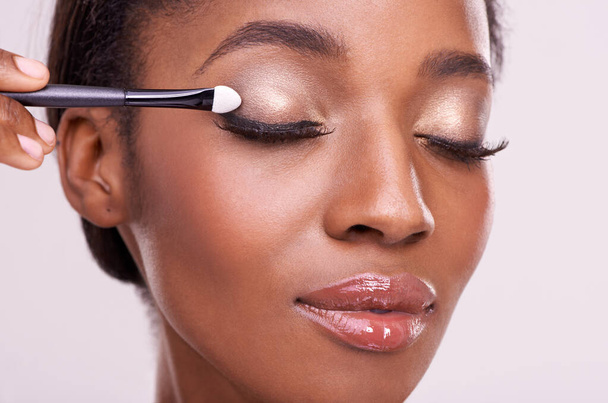 Black woman, face and brush for eyeshadow with makeup, beauty and lashes isolated on pink background. Skin glow, cosmetics product and tools for cosmetology, shimmer or glitter with shine in studio. - Photo, Image
