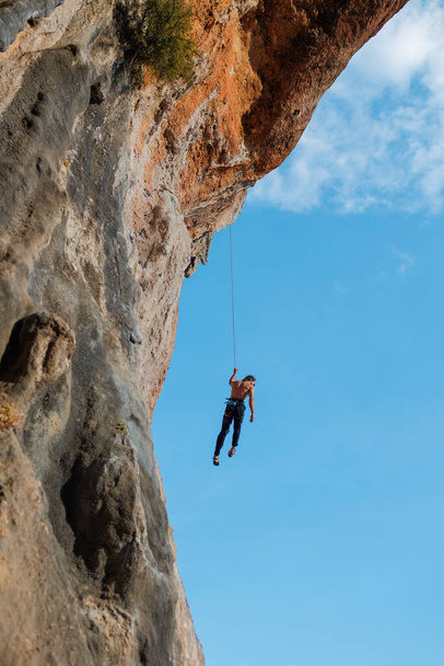 escalador de roca desciende de una ruta, un escalador cuelga de una cuerda contra el cielo, rutas de escalada en roca en una cueva, un hombre rappel por una cuerda - Foto, imagen