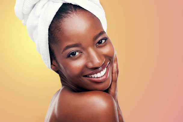 Portret, uśmiech i czarna kobieta z ręcznikiem do włosów w studio do pielęgnacji skóry, wellness lub pielęgnacji ciała na pomarańczowym tle. Piękno, czyszczenie i twarz afrykańskiej modelki z kosmetykiem, połyskiem lub miękką skórą. - Zdjęcie, obraz